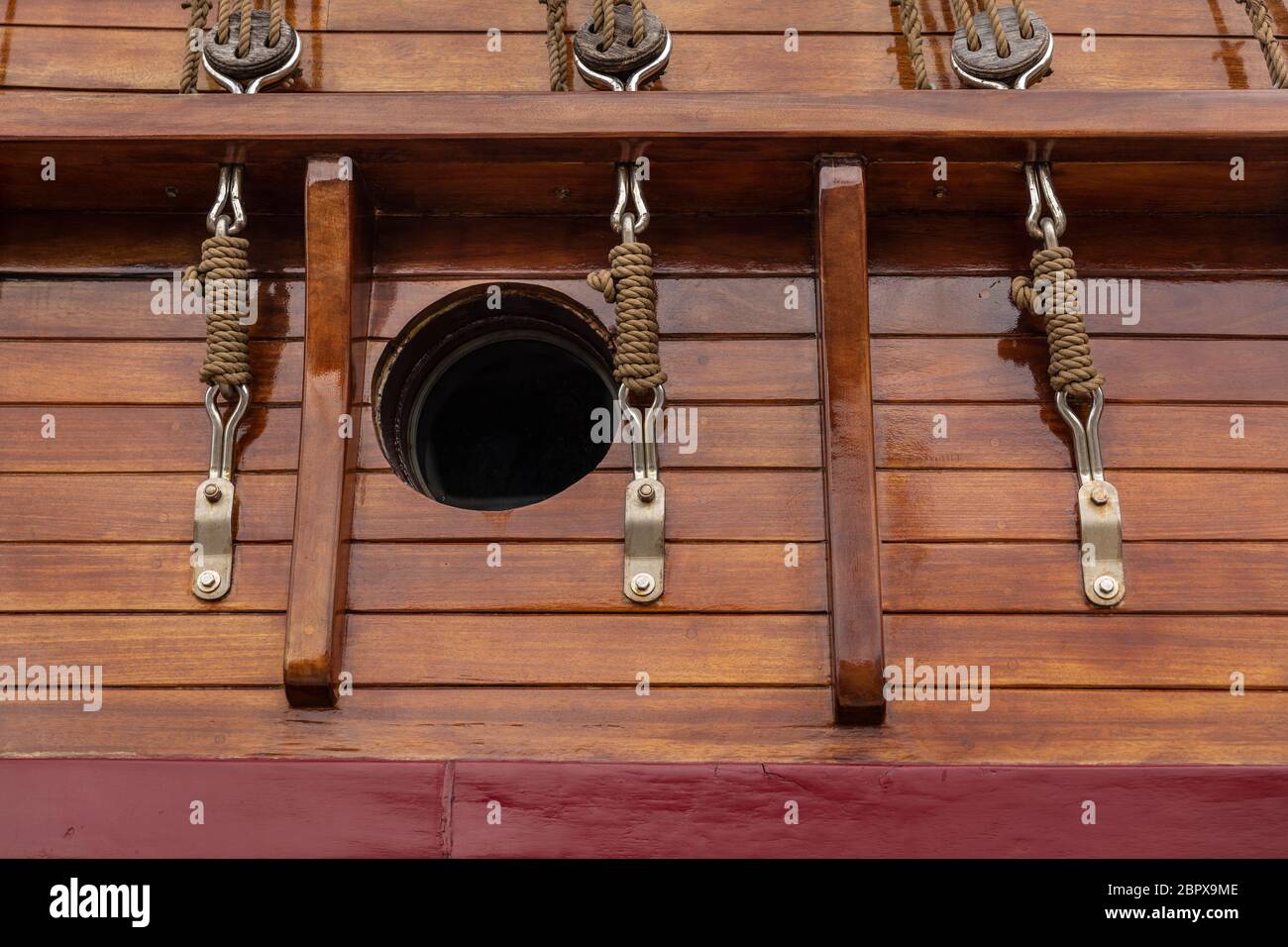 Un hublot et des blocs de poulie avec des cordes dans un style ancien sur un bateau à voile historique. Matériaux en bois de teinte chaude pour une sensation rétro Banque D'Images