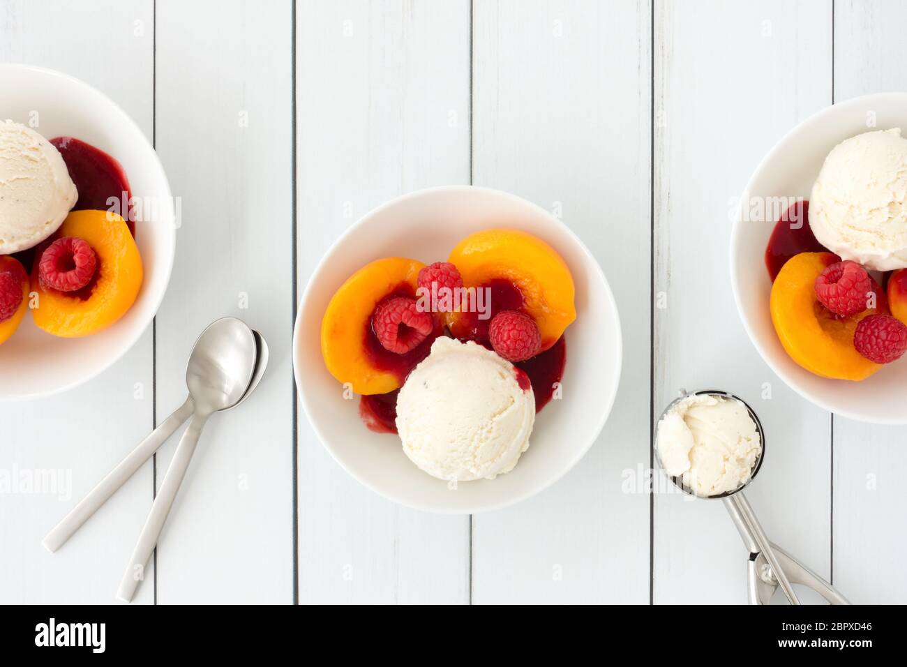 Bols remplis de crème glacée à la vanille, pêches, framboises et sauce à la framboise sur fond de panneau en bois blanc avec espace pour les copies. Vue de dessus. Banque D'Images