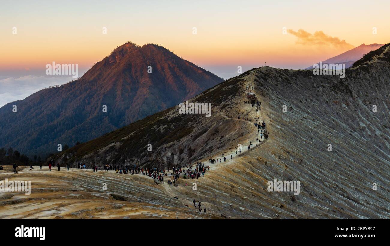 Les gens regardent le lever du soleil depuis le bord du cratère du volcan actif Ijen avec de la fumée de fond. Banque D'Images