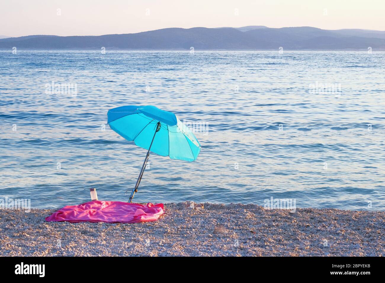 Parasol bleu sur la côte estivale. La plage de mer avec parasol attend les touristes au coucher du soleil. Concept de vacances d'été heureux. Banque D'Images