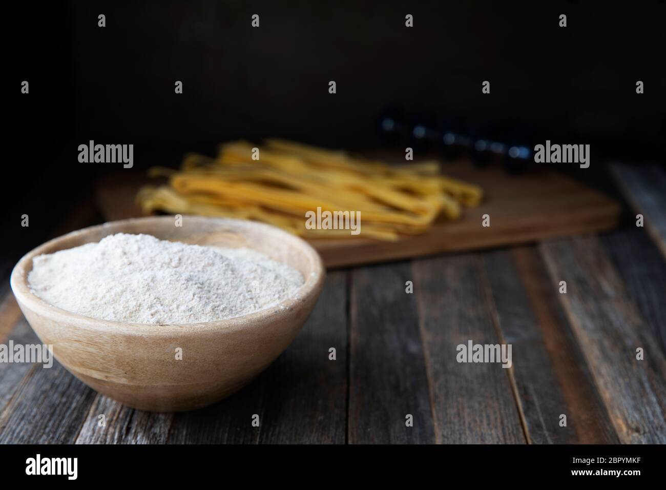 Bol de farine de blé entier sur une table en bois rustique avec des pâtes pappardelle en arrière-plan. Banque D'Images