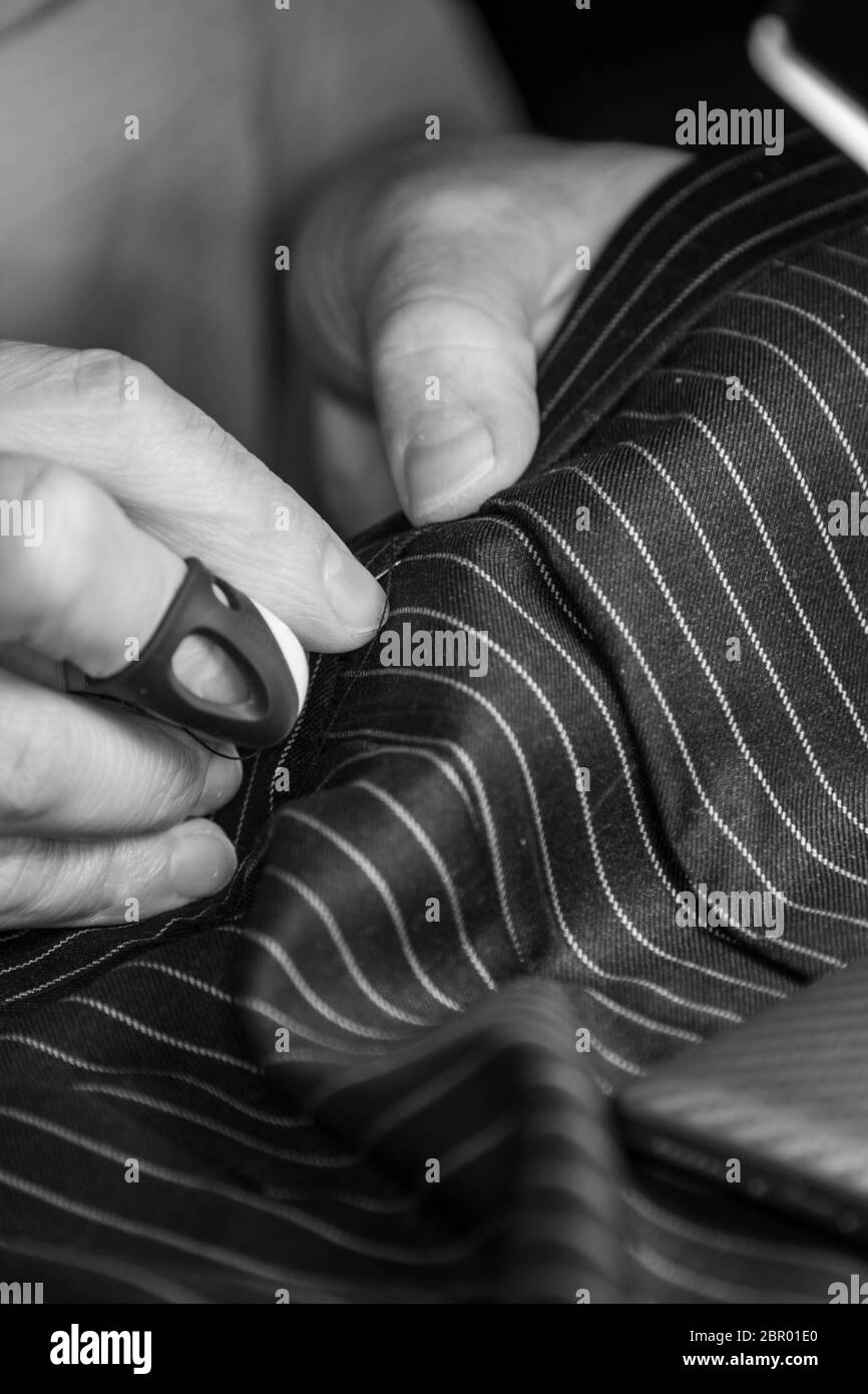 Noir et blanc gros plan mains de couturière au travail avec tissu. Main de travail couture pantalon avec aiguille et fil Banque D'Images