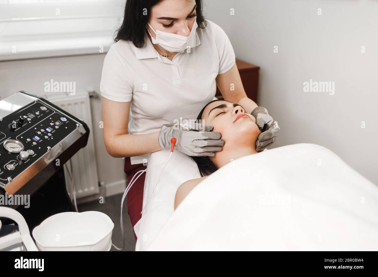 Traitement par microcourant. Le cosmologiste fait un massage stimulant du visage avec des gants électriques. Massage du drainage lymphatique Banque D'Images