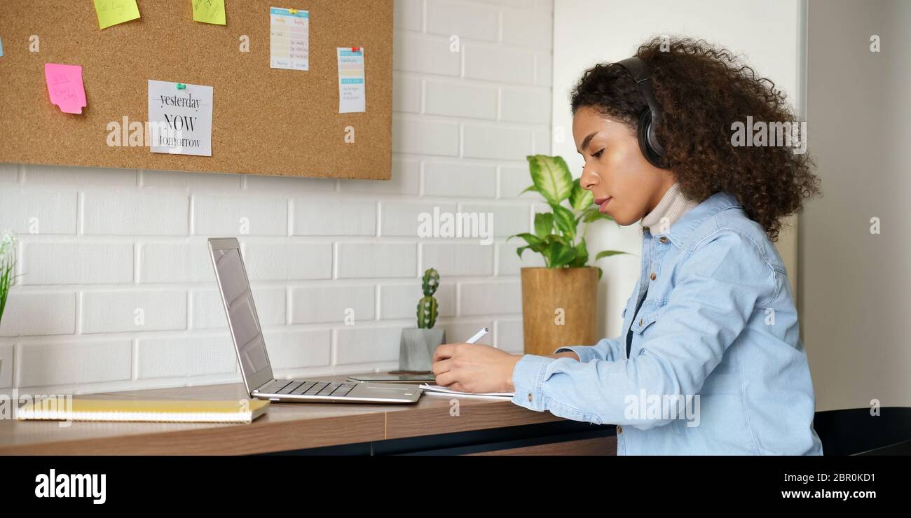 Afrique adolescent fille étudiant porter des écouteurs regarder le séminaire en ligne de prendre des notes. Banque D'Images