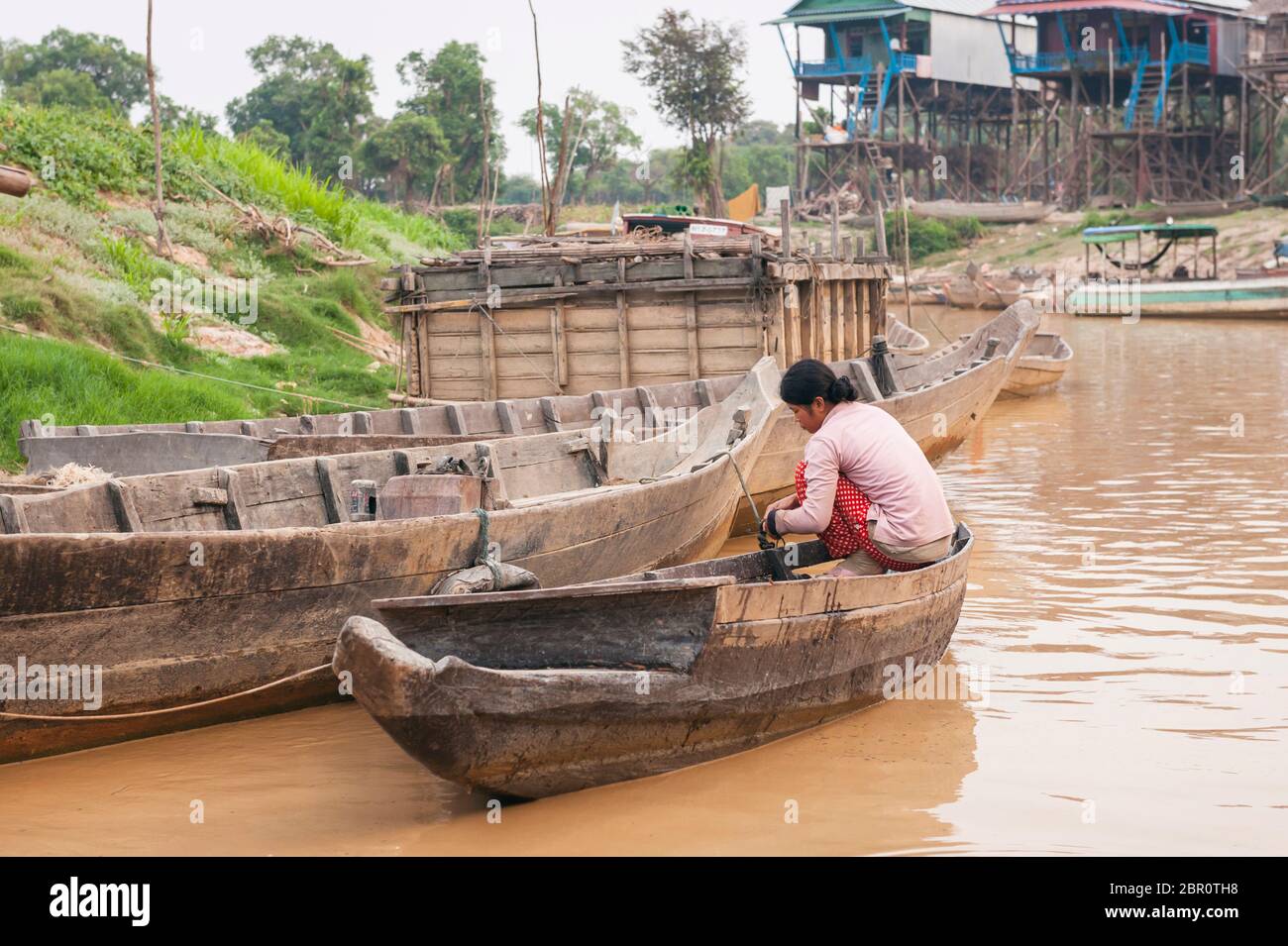 Une femme cambodgienne sur un bateau sur le fleuve avec des maisons sur pilotis en arrière-plan à Kampong Phluk, province de Siem Reap, centre-nord du Cambodge. Banque D'Images