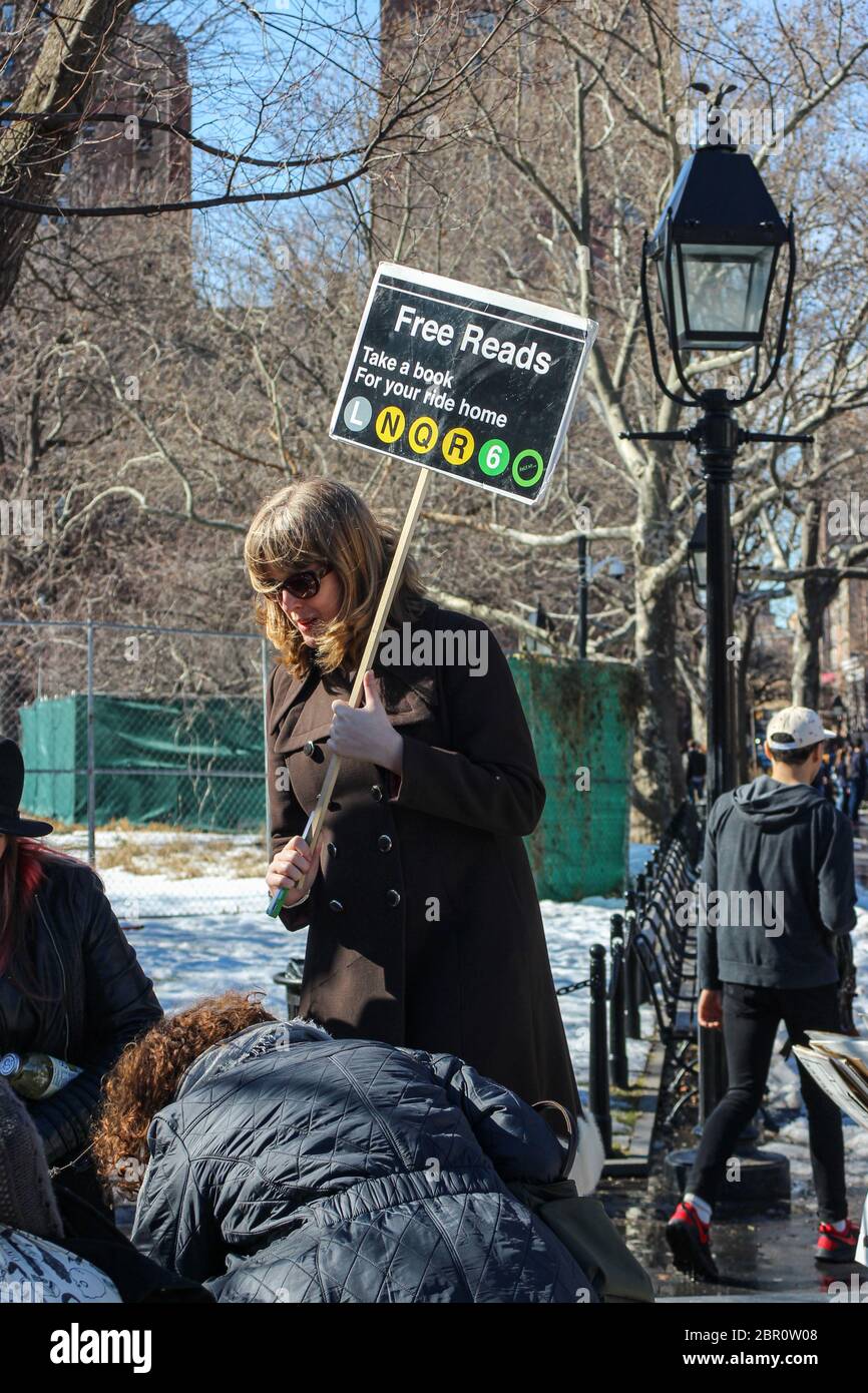 Femme d'âge moyen tenant un écriteau Free Reads et donnant des livres usagés à Washington Square Park de Manhattan, New York City, États-Unis Banque D'Images