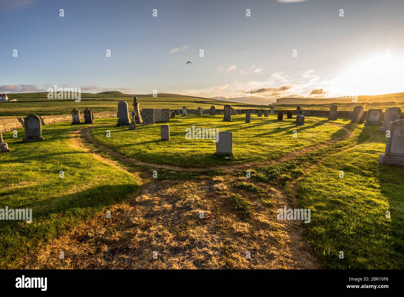 Vieux cimetière perché plein de pierres tombales sur le Shetland (Écosse, Royaume-Uni) sur un coucher de soleil panoramique avec lumière chaude spectaculaire et herbe verte illuminée Banque D'Images