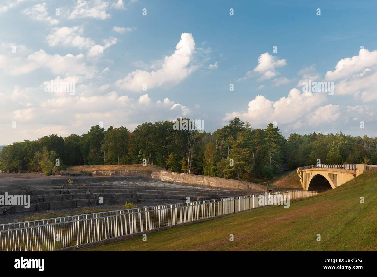 Réservoir d'Ashokan débordement avec pont, herbe roulante, arbres, ciel bleu avec nuages et clôture métallique à l'heure d'or. Banque D'Images