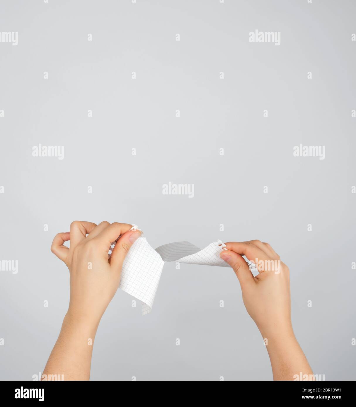 Deux mains déchirer dans la moitié d'une feuille de papier blanc, fond gris Banque D'Images