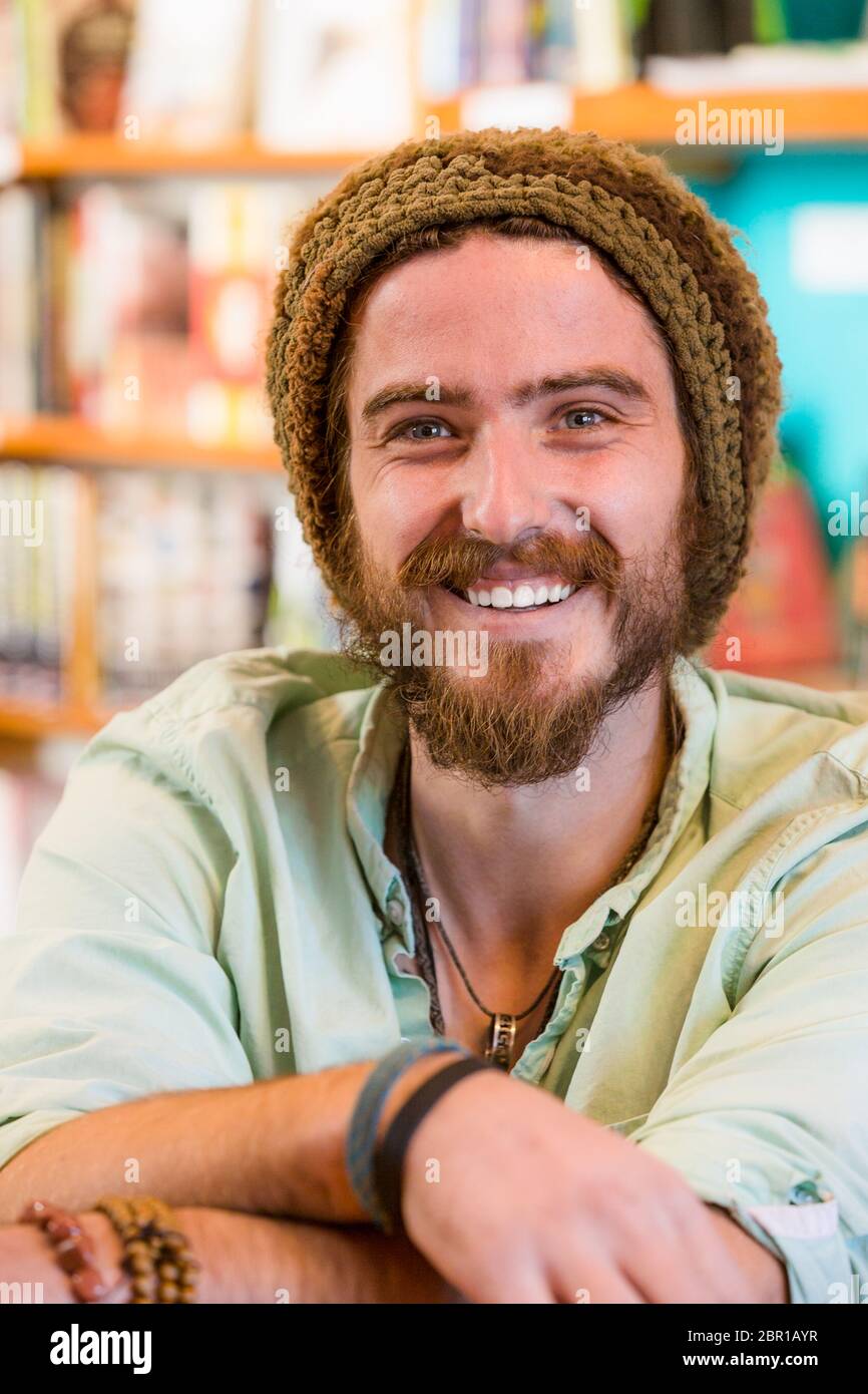 Jeune homme souriant avec bonnet en tricot dans un magasin de livres ou une bibliothèque Banque D'Images