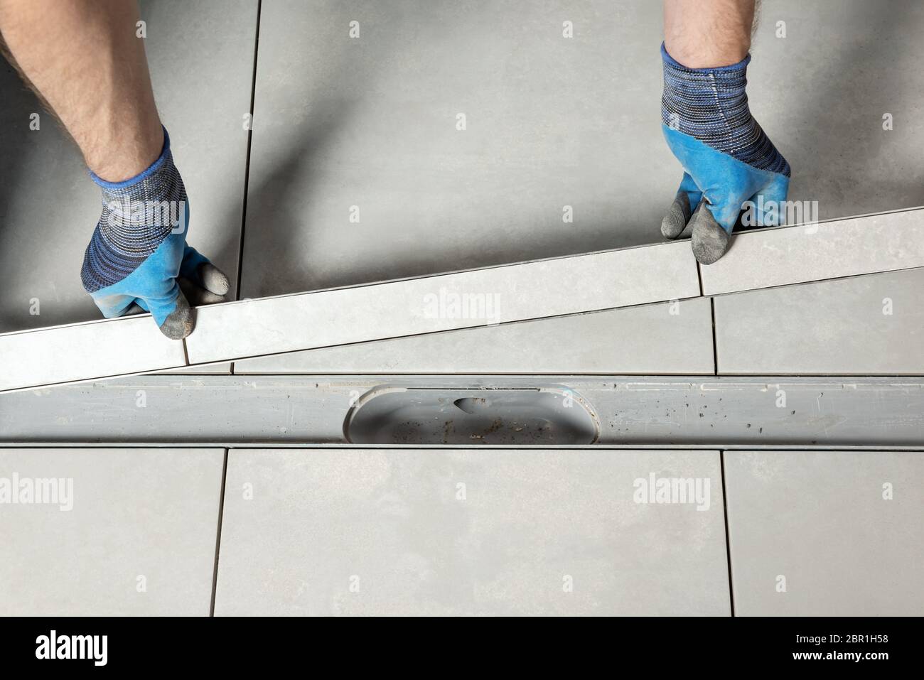 Un ouvrier installe un couvercle d'évacuation décoré de carreaux de céramique dans la salle de bains. Banque D'Images