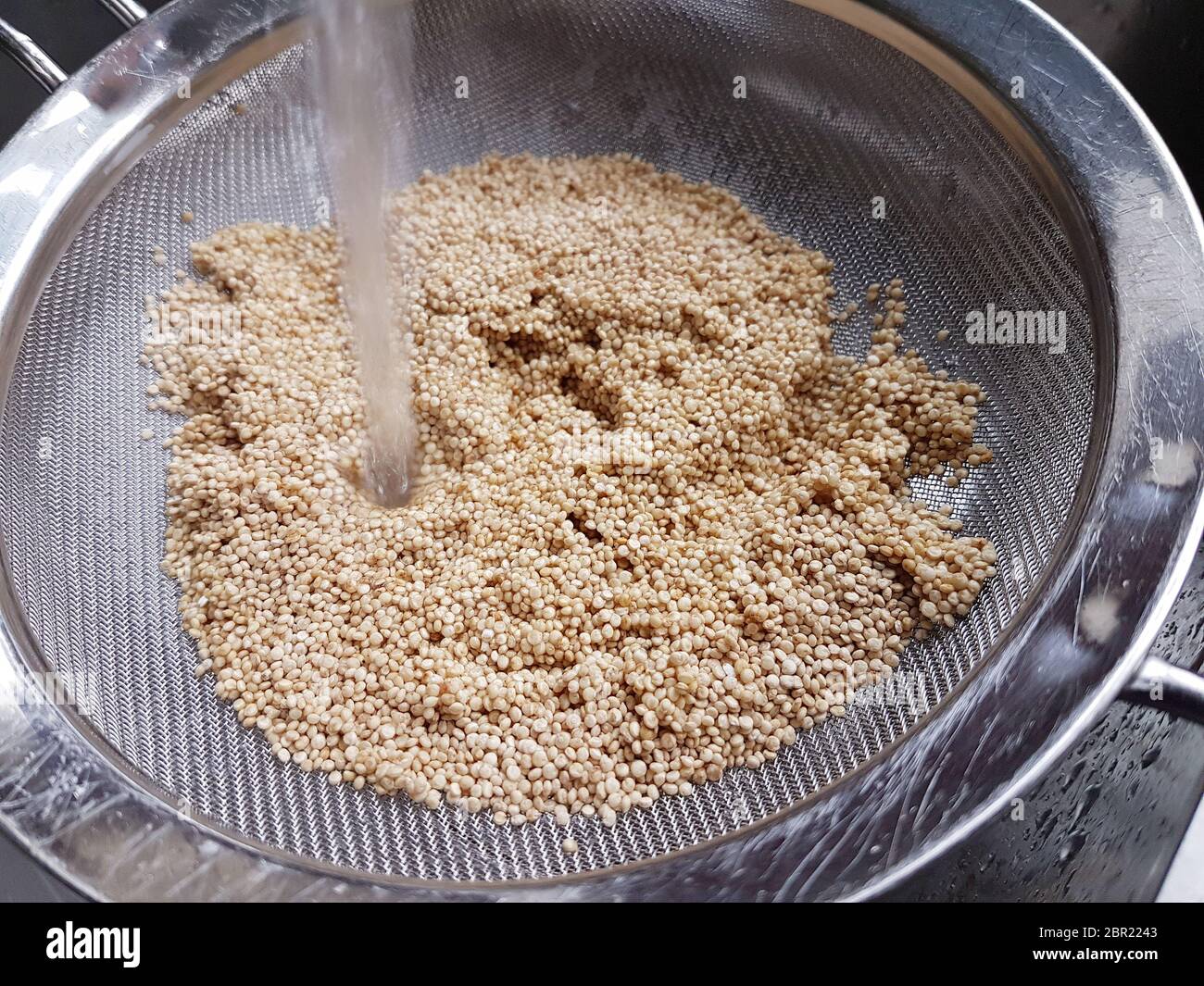 Quinoa non cuit dans un tamis de passoire en fil de fer lavé sous un  robinet Photo Stock - Alamy