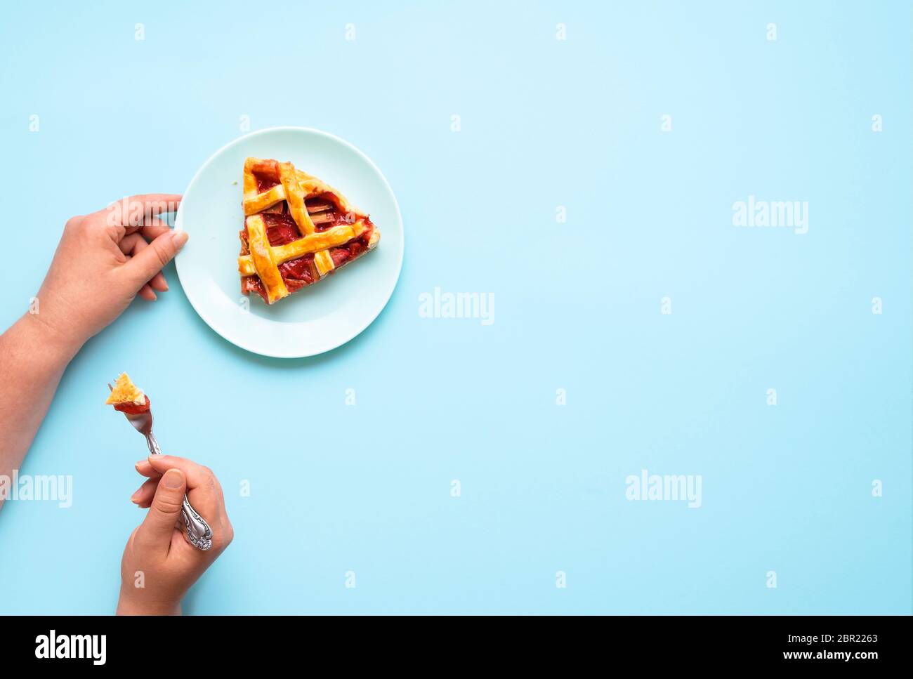 Manger un morceau de rhubarbe et de tarte aux fraises sur fond bleu. Plat de la femme ayant une tranche de gâteau de rhubarbe. Délicieux dessert allemand. Banque D'Images