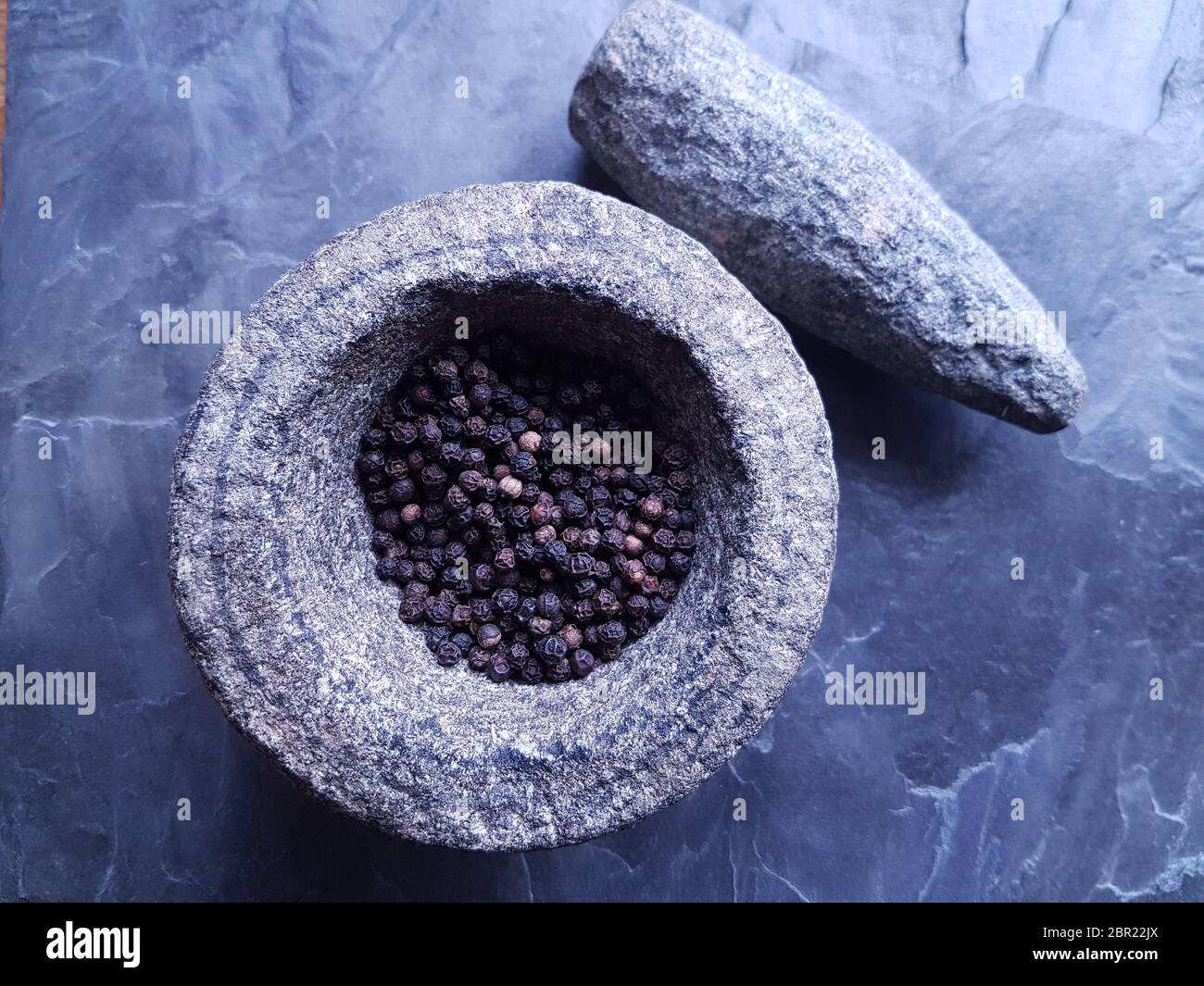 Grains de poivre noir dans un mortier de pierre et pilon sur un fond d'ardoise Banque D'Images