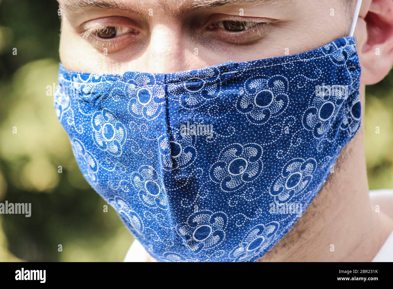 Jeune homme blanc barbu avec un masque facial en tissu bleu pendant une pandémie de coronavirus. Coronavirus, éclosion de COVID-19. Concept de protection contre les virus. Mise au point sélective, fond flou. COV-SRAS-2. Banque D'Images