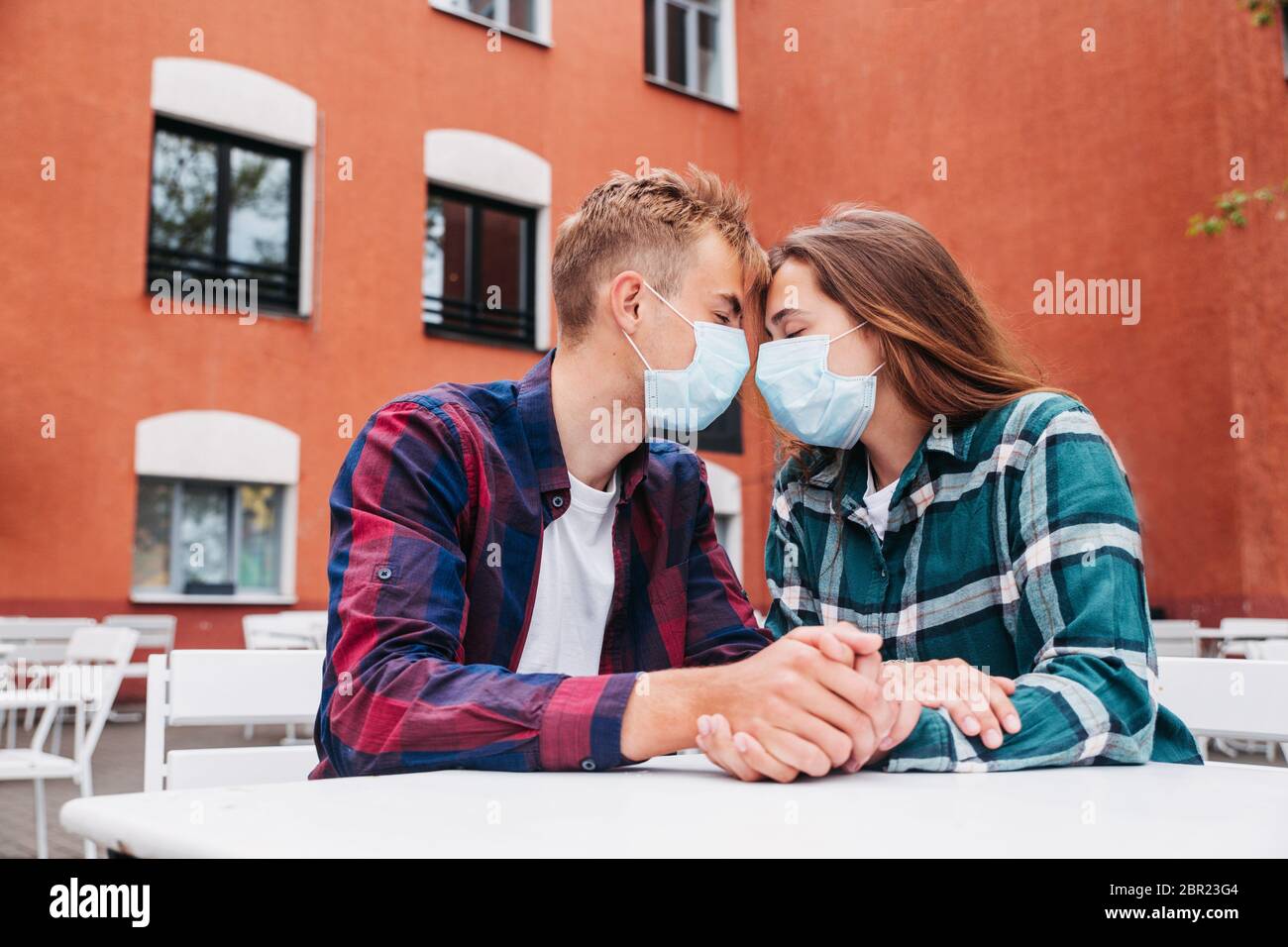 Couple amoureux, homme et femme s'embrassant dans un masque médical protecteur sur le visage, Focus sur les mains Banque D'Images