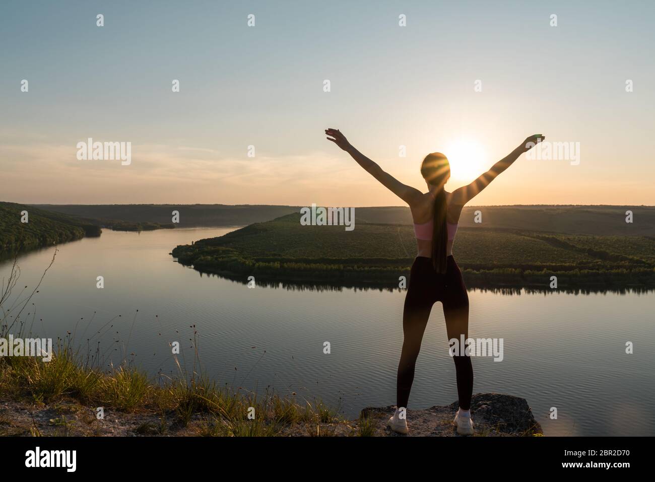 Silhouette d'une jeune femme sportive debout sur une crête, profitant du coucher de soleil sur une vallée de rivière Banque D'Images