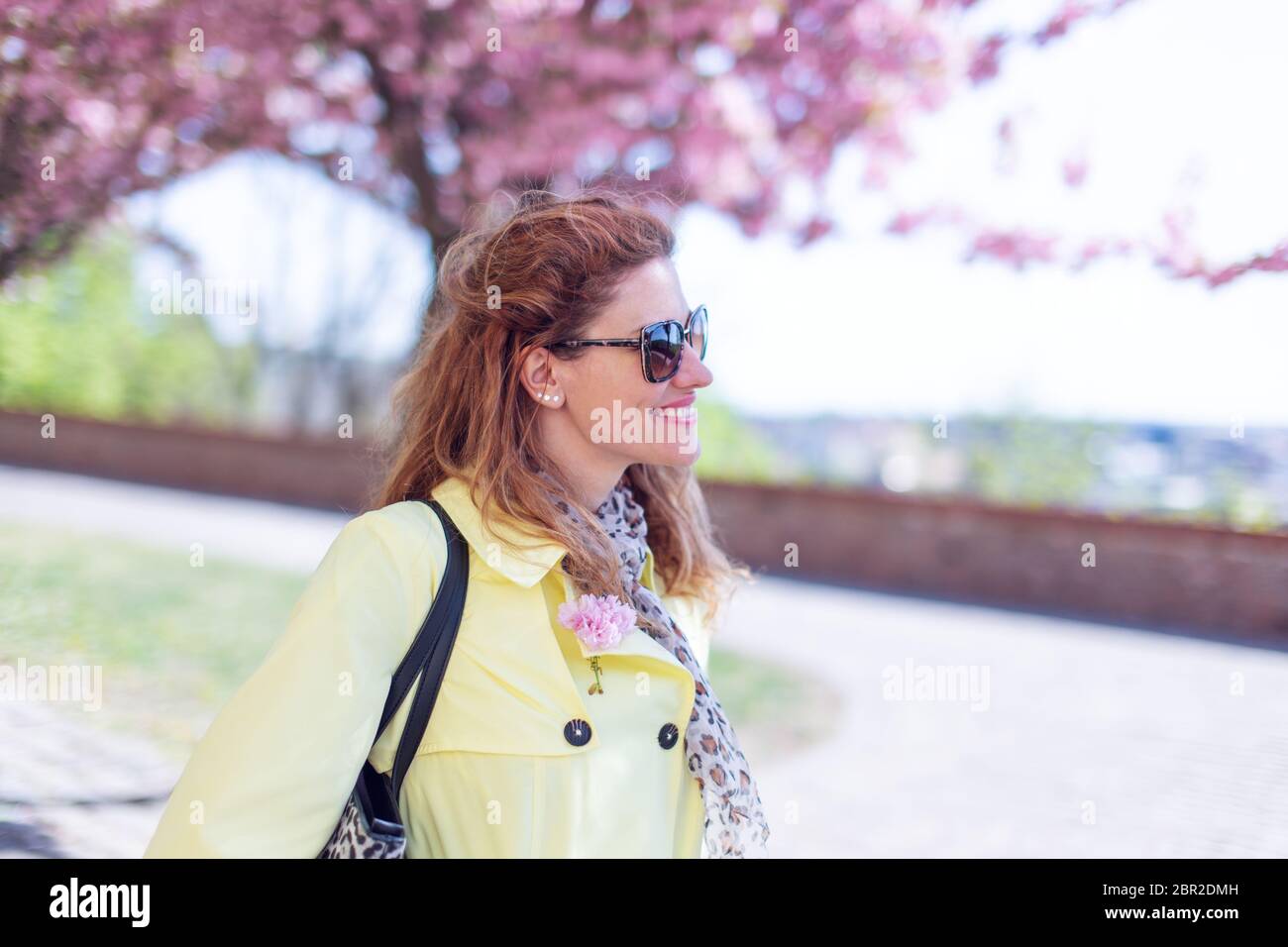 Jeune femme à tête rouge dans le parc marchant au printemps Sakura, sourire en dents de souris Banque D'Images