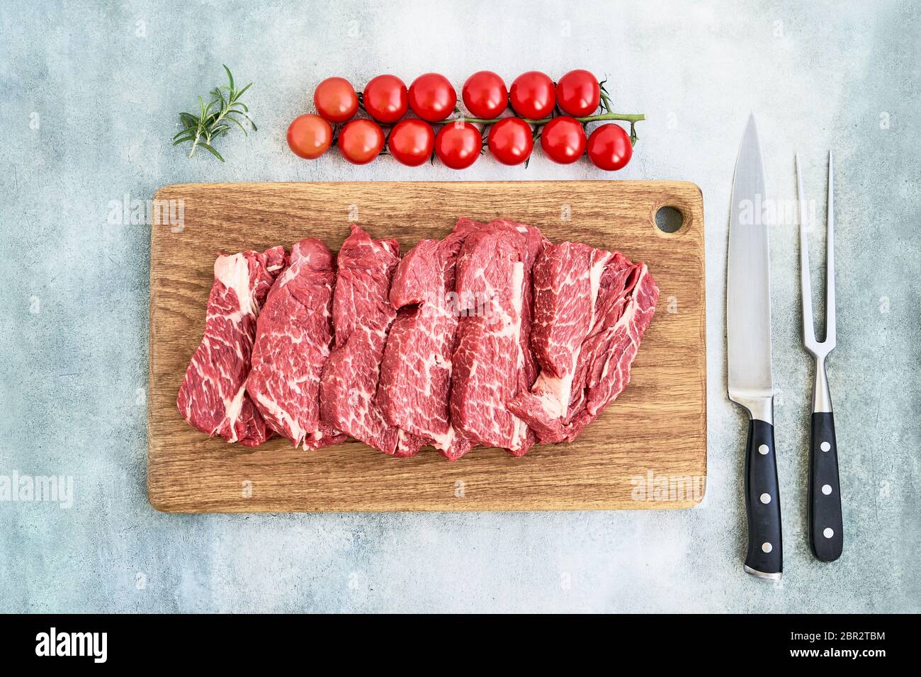 Steaks de bœuf frais crus au poivre et aux tomates sur planche à découper en bois sur fond bleu. Espace de copie, vue de dessus. Banque D'Images