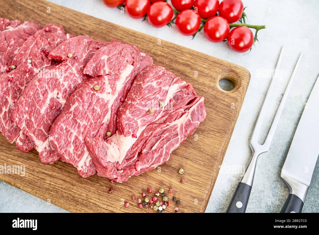 Steaks de bœuf frais crus avec poivre et tomates sur la planche à découper Swooden. Vue de dessus Banque D'Images