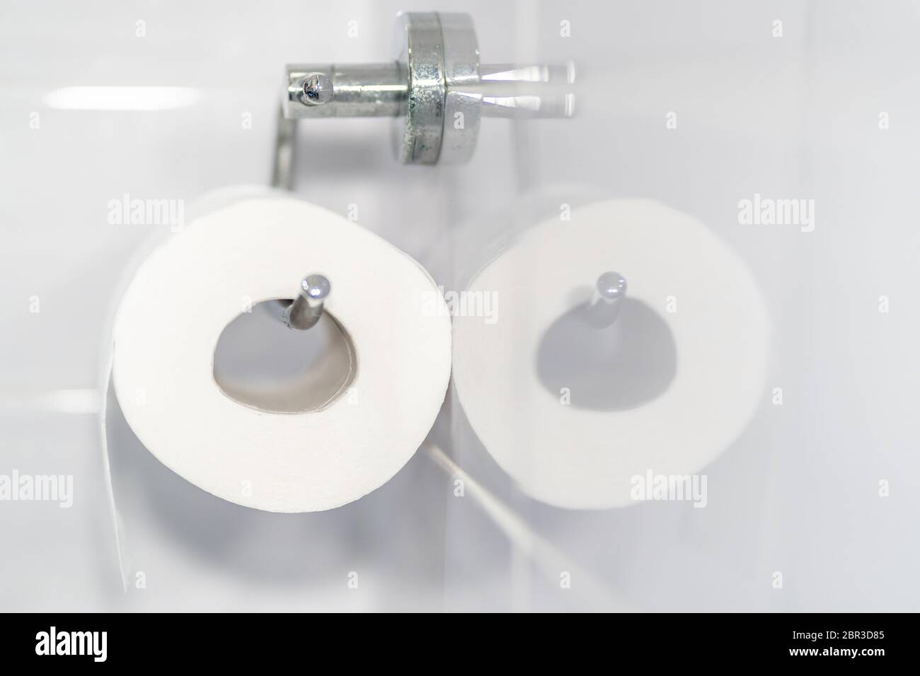 Gros plan d'un rouleau de papier toilette blanc et doux accroché à un support moderne en chrome dans une salle de bain lumineuse. Se reflète dans le carrelage de la salle de bains. Banque D'Images
