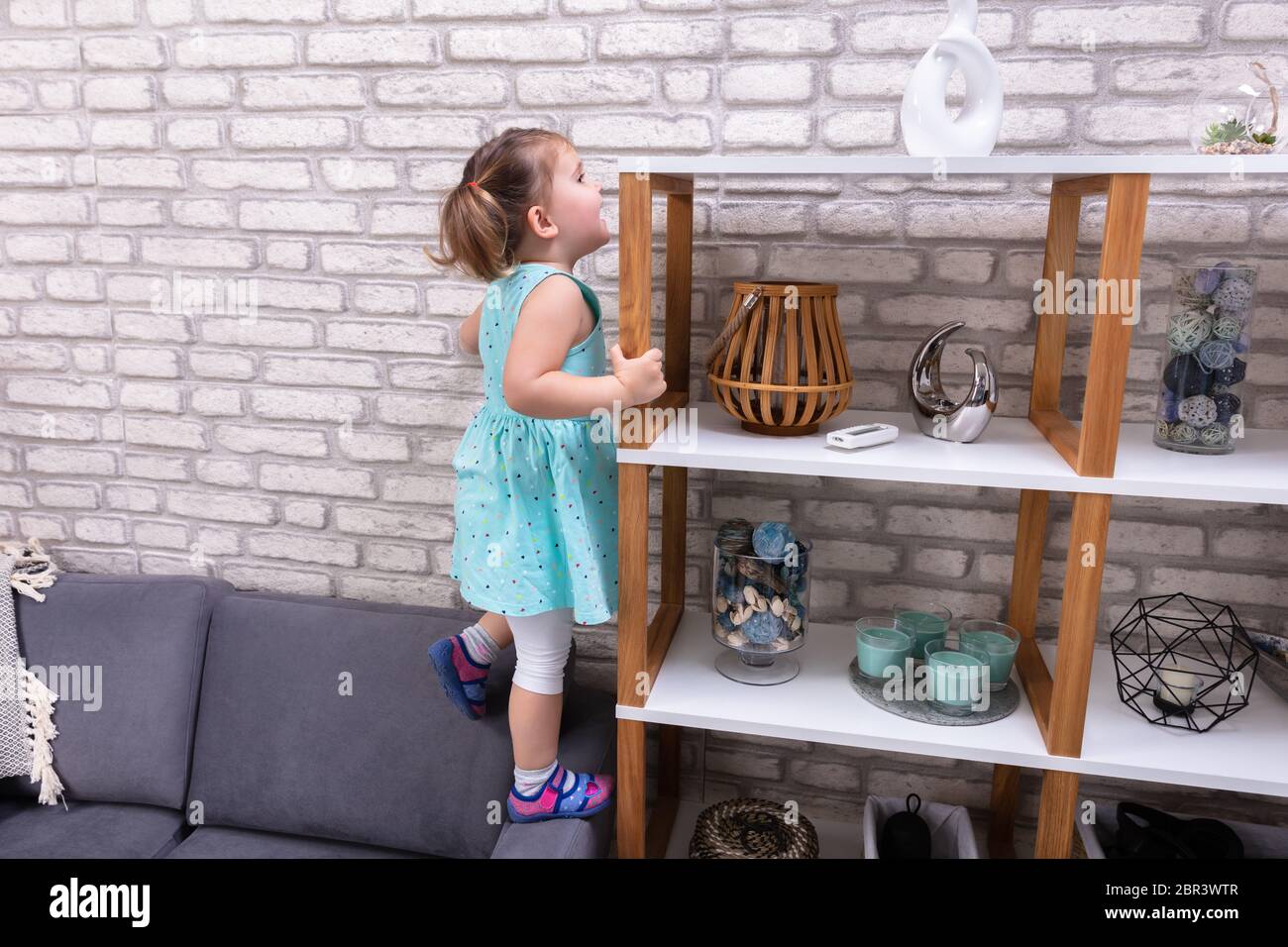 Mignon Bebe Fille Debout Sur Un Canape Et D Atteindre Pour Les Jouets Sur Une Etagere Photo Stock Alamy