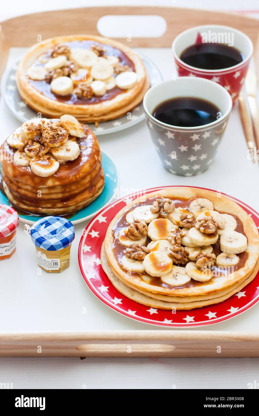 Plateau de petit déjeuner avec crêpes aux bananes, sirop d'érable et noix, tasse de café et miel. Concept de la nourriture du matin. Banque D'Images Plateau de petit déjeuner avec crêpes aux bananes, sirop d'érable et noix, tasse de café et miel. Concept de la nourriture du matin. Banque D'Images