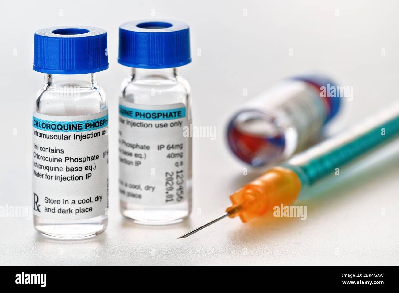Chloroquine phosphate dans de petits flacons d'injection avec bouchons bleus, seringue orange verte près, détail de gros plan (conception de l'étiquette avec données fictives - non Banque D'Images