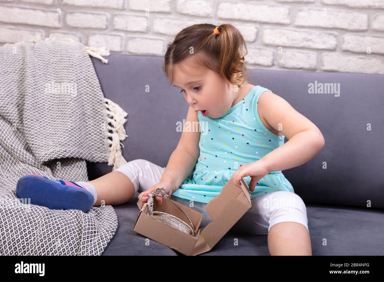 Surprise Petite fille assise sur le canapé marron ouverture boîte à colis Banque D'Images