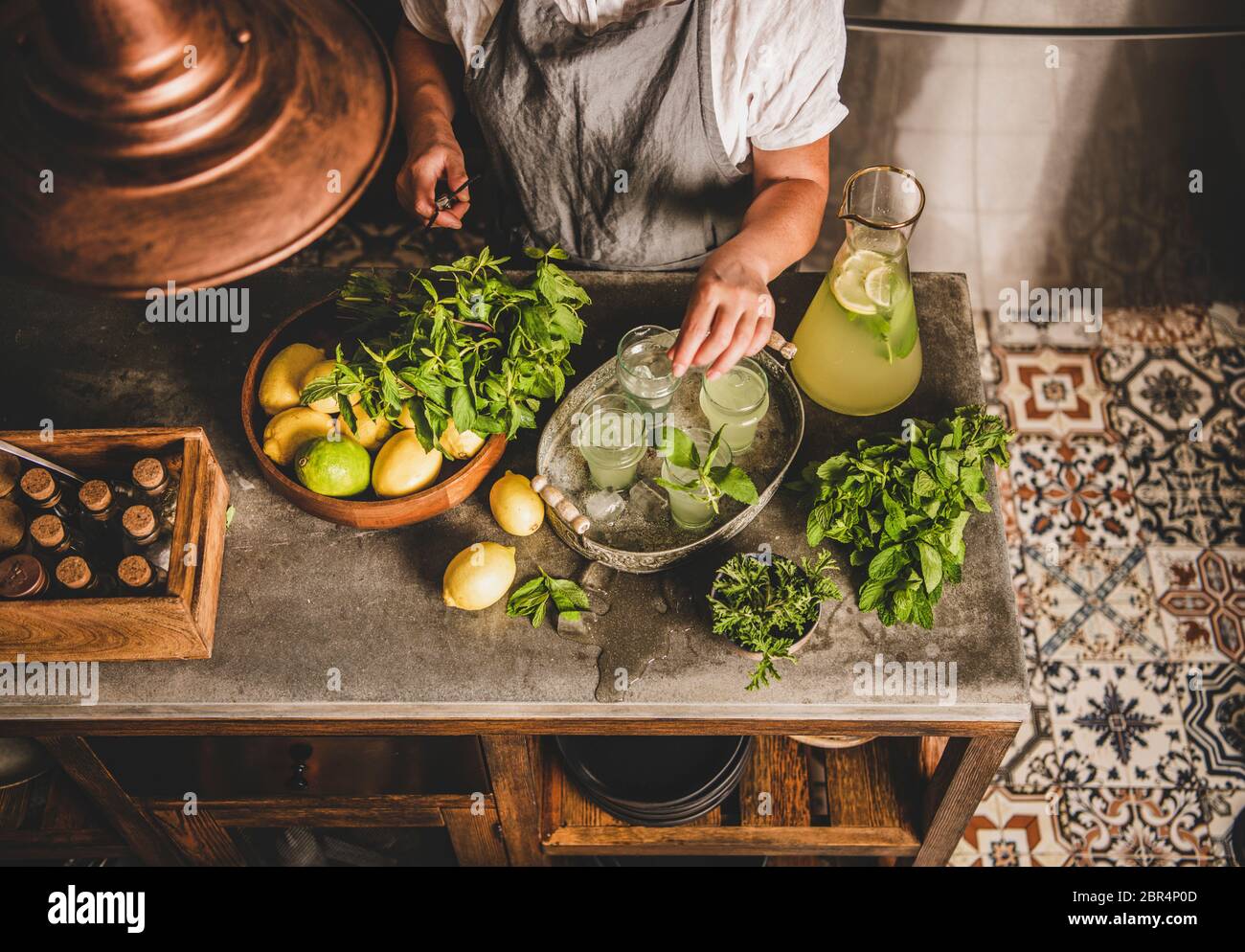 Mains de femme faisant de la limonade maison fraîche sur un comptoir de cuisine en marbre. Femme ajoutant de la menthe fraîche à la limonade froide avec du citron et de la glace dans des verres en r Banque D'Images