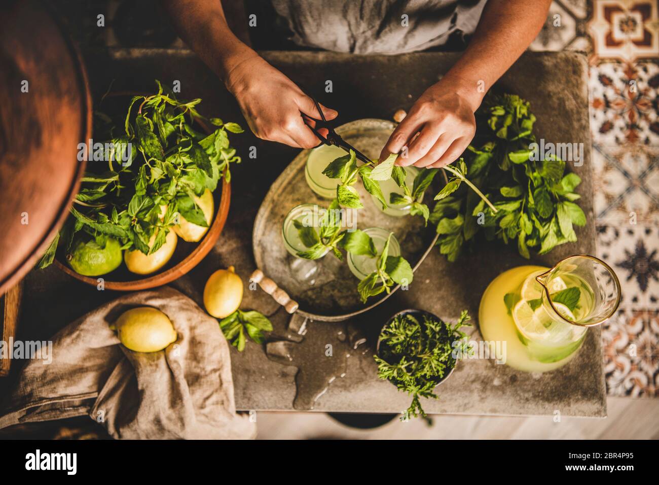Mains de femme faisant de la limonade maison fraîche. Femme décorant la limonade froide aux agrumes dans des verres avec des feuilles de menthe fraîche sur le marbre gris cuisine counte Banque D'Images