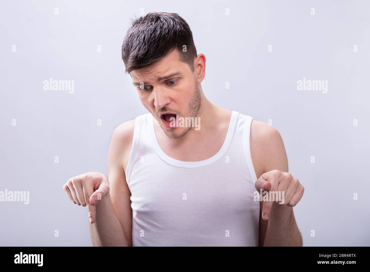 Choqué Homme en blanc Tanktop pointant son doigt vers le bas contre l'arrière-plan blanc Banque D'Images