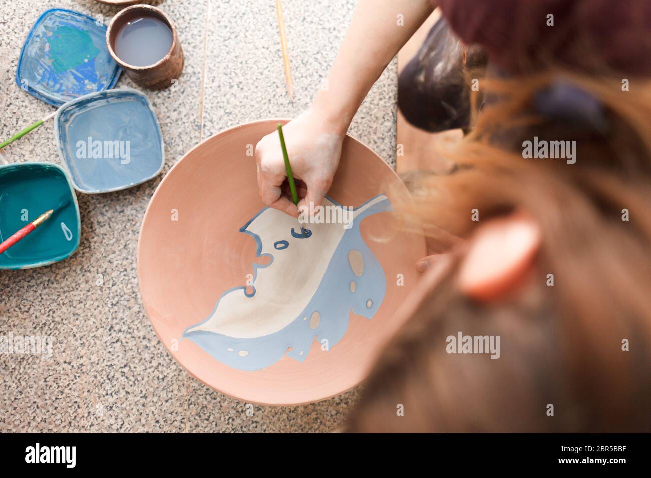 Potter femme peint une plaque en céramique. Fille tire avec un pinceau sur la faïence. Processus de création de produits d'argile. Banque D'Images