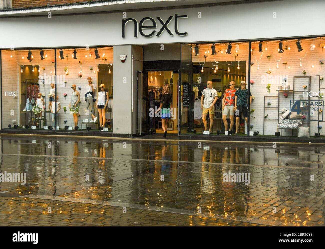 SWANSEA, PAYS DE GALLES - JUILLET 2018 : personne entrant dans une succursale de Next dans le centre-ville de Swansea. Les lumières de l'atelier se reflètent dans le sol humide après la pluie Banque D'Images