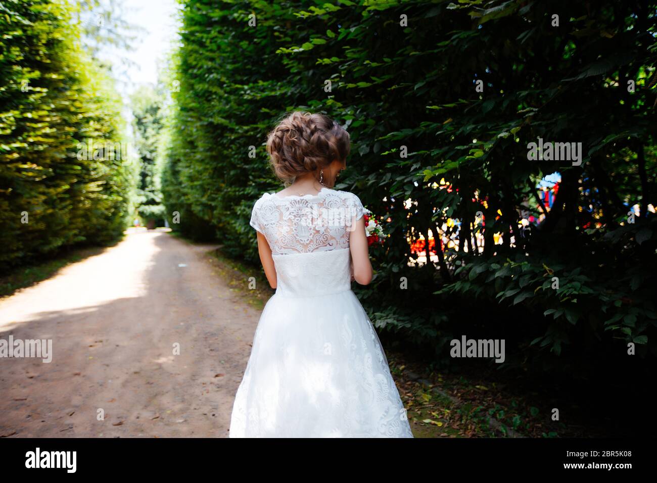 La mariée dans une robe de mariage blanche tient un bouquet sur un fond de parc vert Banque D'Images
