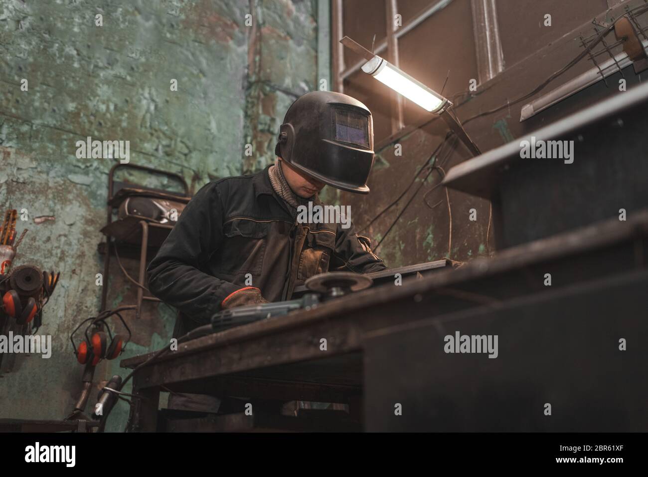 Un travailleur dans un masque de soudeur travaille dans un atelier pour le soudage du fer. L'homme fabrique des produits en fer. Guy travaille avec une machine à souder en utilisant un masque pour protéger son ey Banque D'Images