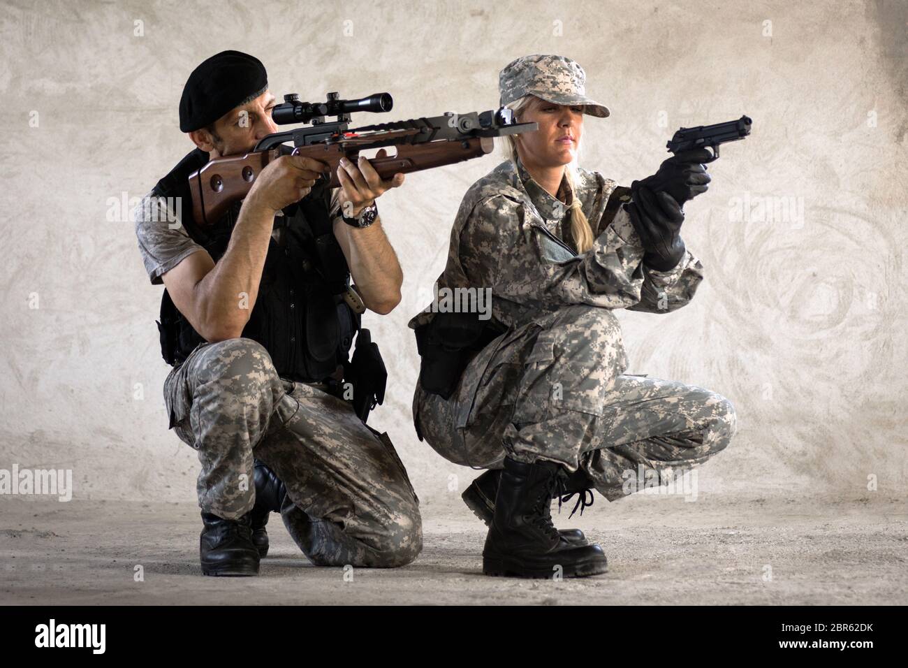 Les soldats hommes et femmes en uniforme militaire visent avec un arc-en-croix et un pistolet et s'écraseront sur fond de mur gris. Banque D'Images