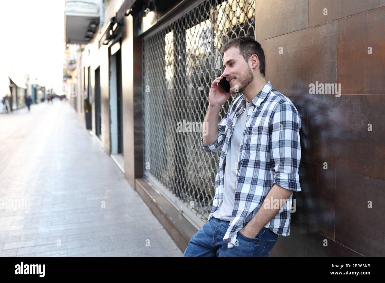 Portrait d'un heureux homme sur un smartphone, en vue latérale, appuyé sur un mur dans la rue Banque D'Images