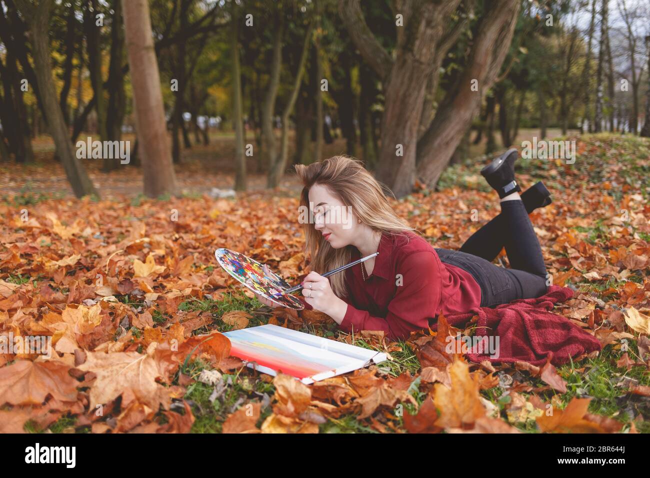 Une jeune artiste se détende dans le parc pour son passe-temps préféré. Fille dessine une image, tenant une palette à la main Banque D'Images