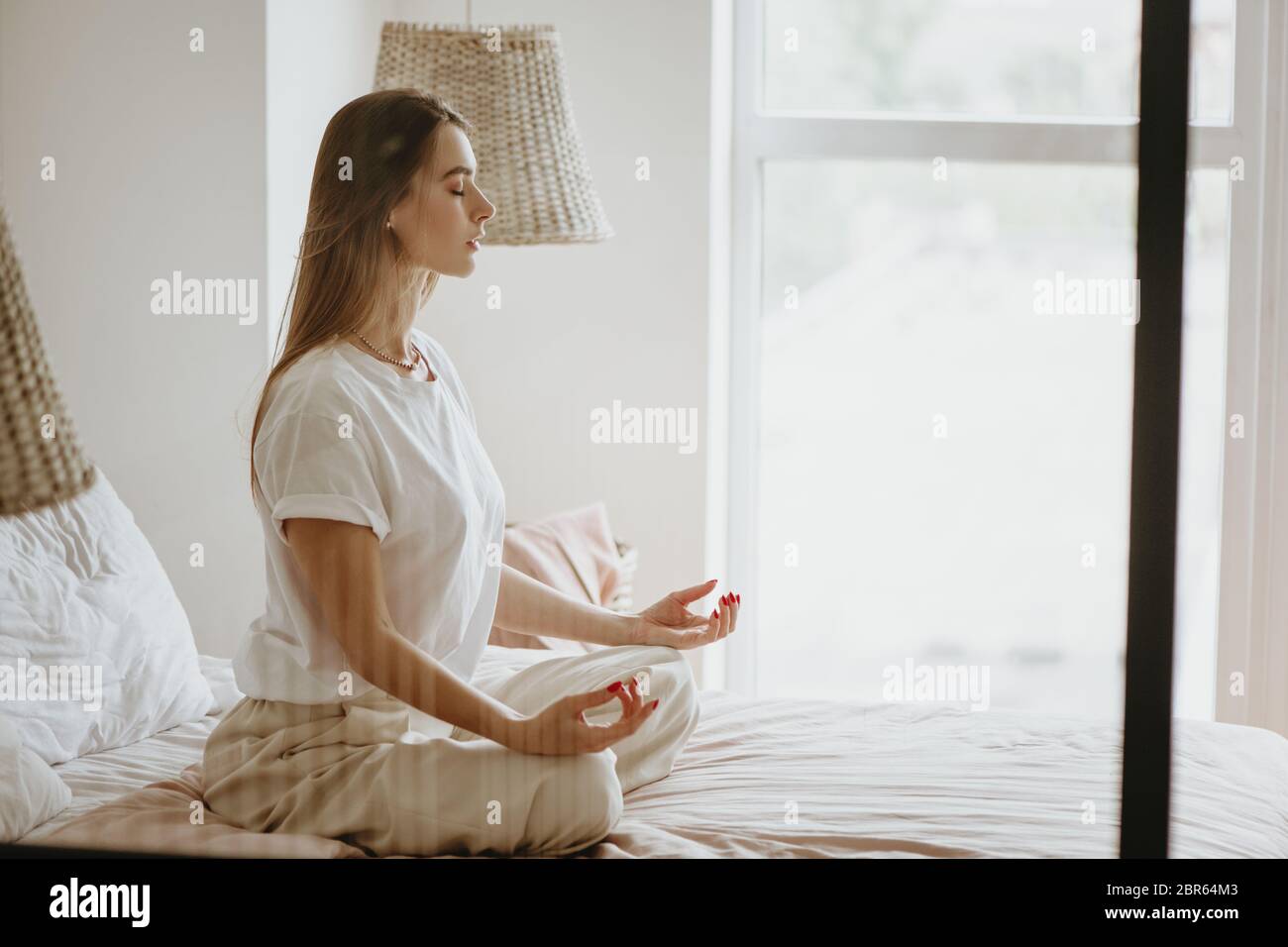 Belle jeune femme pratiquant la méditation sur le lit à la maison. Banque D'Images