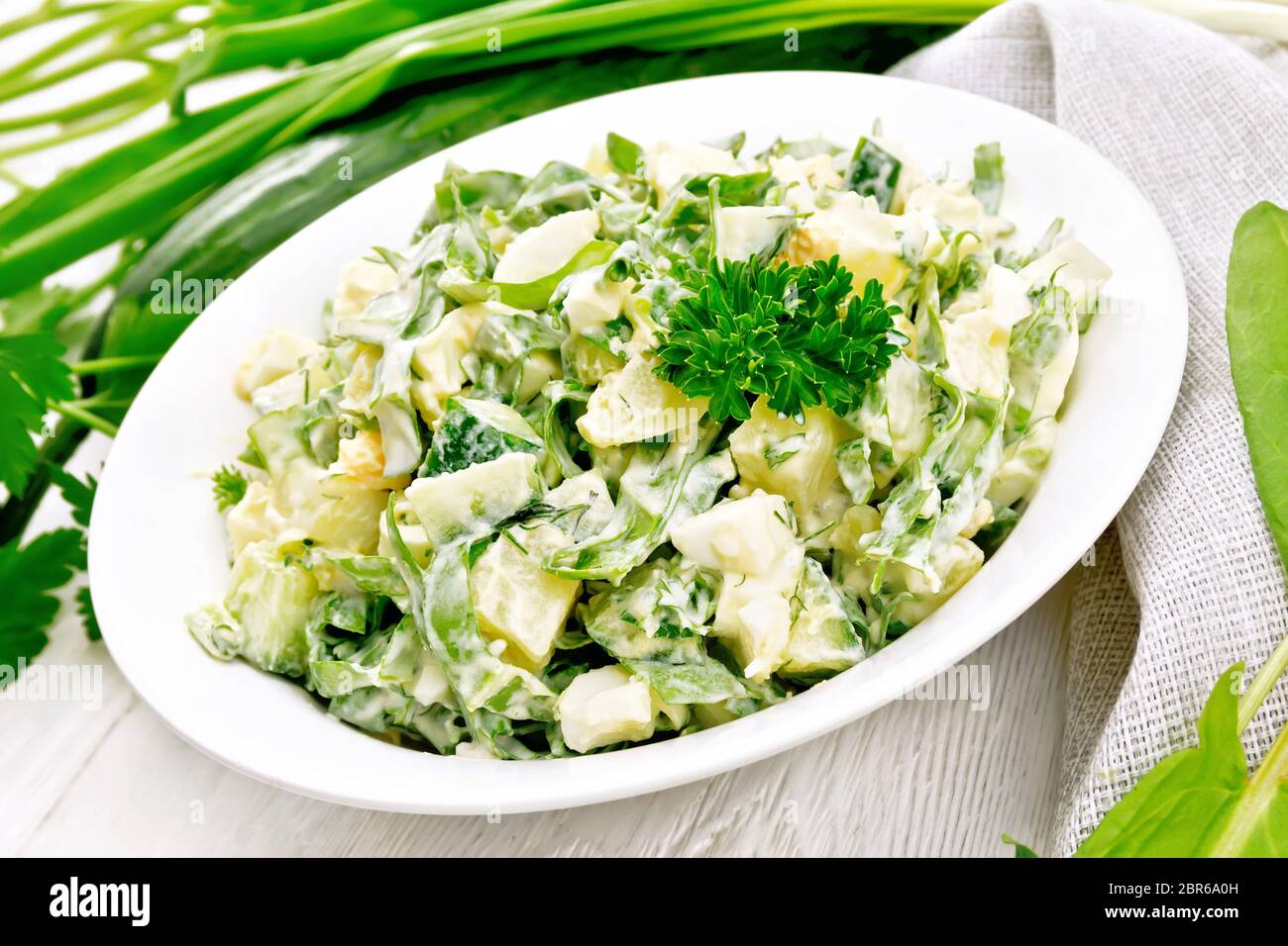 Salade de concombre, oseille, pommes de terre bouillies, les oeufs et les herbes, habillé avec de la mayonnaise en plaque blanche, le persil, les oignons verts et une serviette contre le backg Banque D'Images