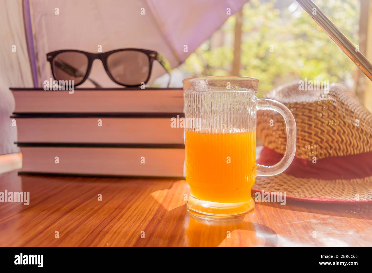 Super protection contre le soleil. Concept de risque de coup de soleil. Parapluie protégeant les belles choses de femme. Livres, lunettes de soleil, jus d'orange et chapeau de paille. Somme Banque D'Images