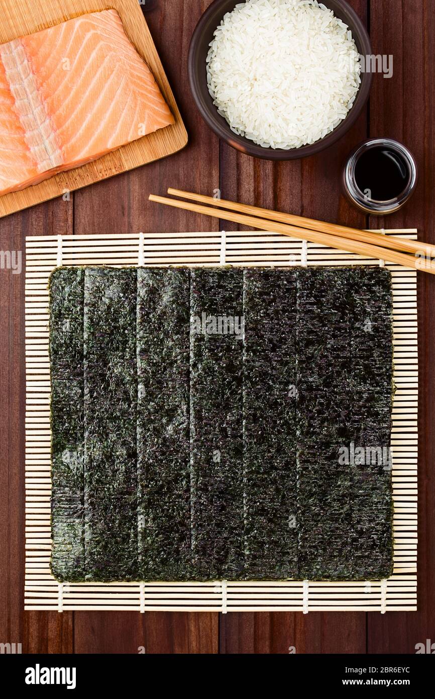 Ingrédients Sushi makisu, d'algue nori sur le tapis de bambou pour le  matériel roulant, du saumon cru frais, crus du riz à sushi, sauce soja et  baguettes sur le côté, photographe Photo