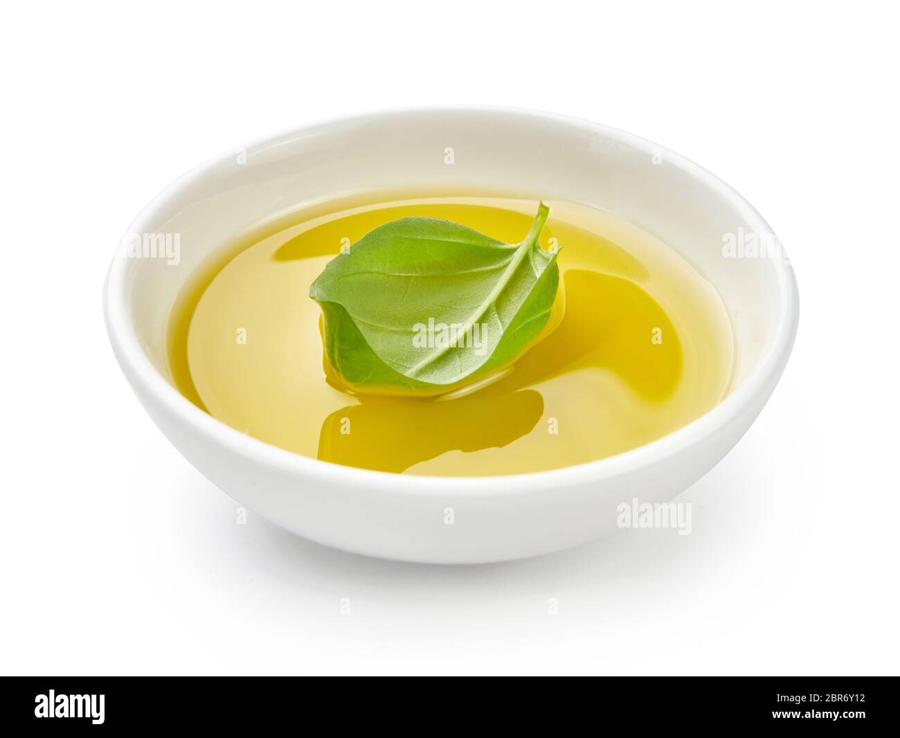 Huile d'olive ou végétale dans un bol blanc. Huile avec feuilles de basilic isolées sur fond blanc. Banque D'Images