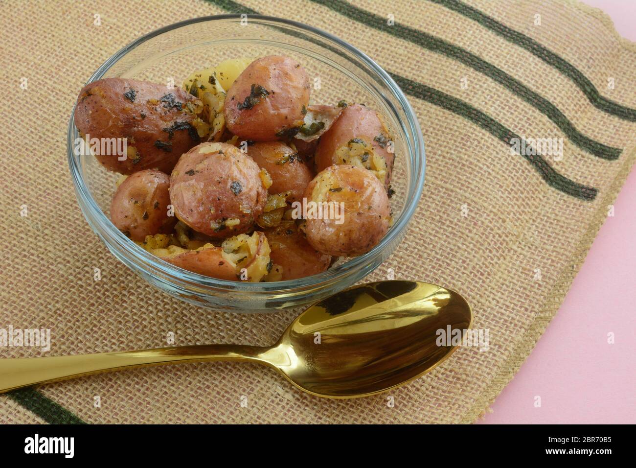 Accompagnement de pommes de terre neuves rouges cuites avec épices dans un bol en verre avec une cuillère de service dorée Banque D'Images