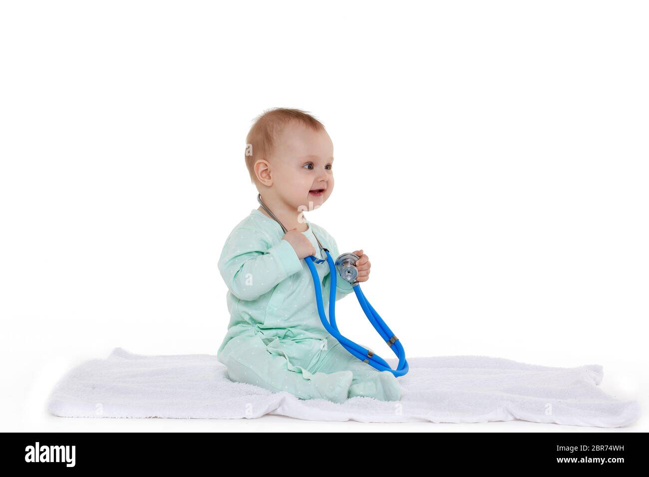 Bébé doux portant une barboteuse verte avec un stéthoscope bleu sur fond blanc. Huit mois Banque D'Images