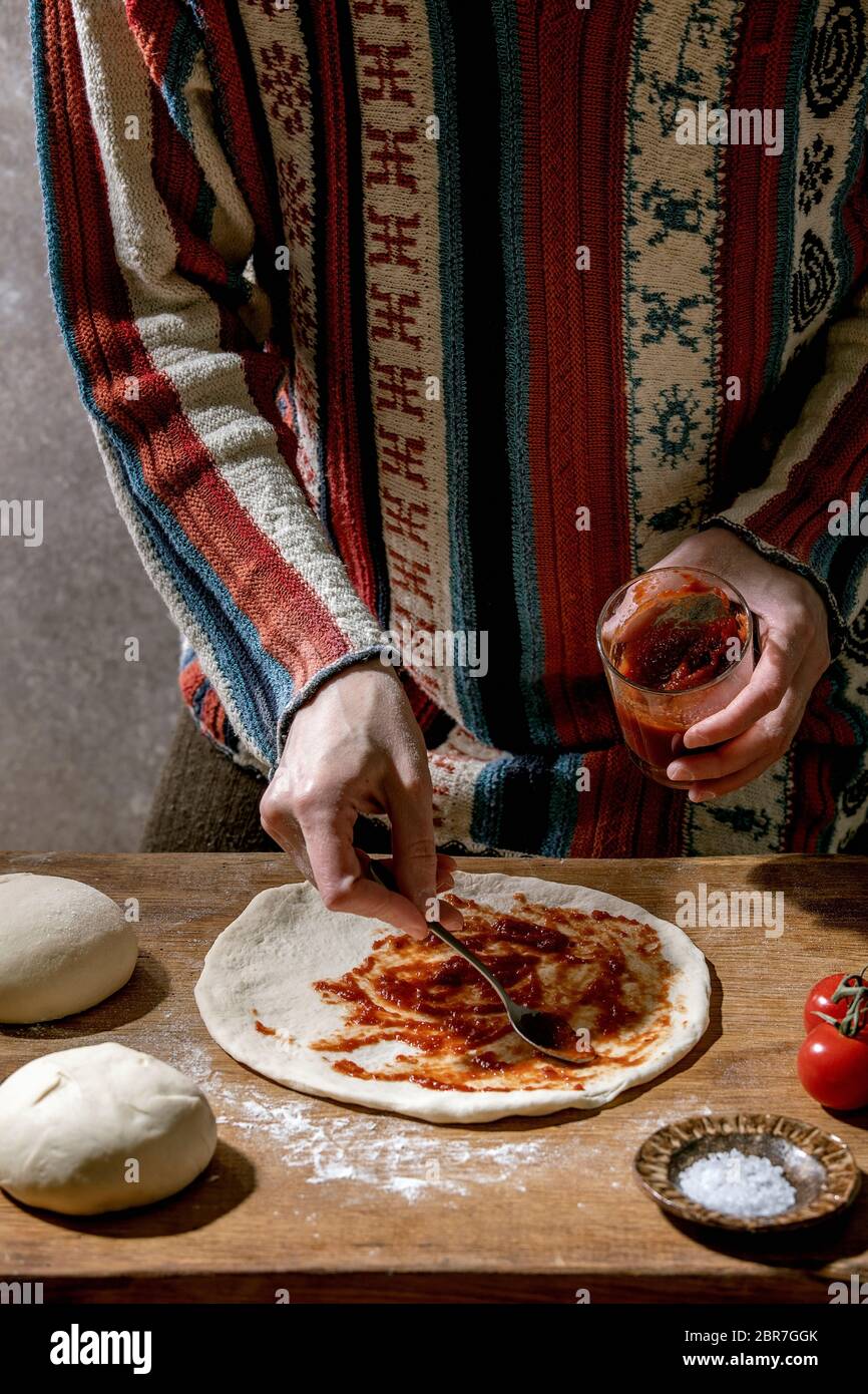 Femme en pull cuisant pizza italienne napolitana. Étaler la pâte de blé  maison fraîche avec sauce tomate. Ingrédients dans les plaques de céramique  ci-dessus Photo Stock - Alamy