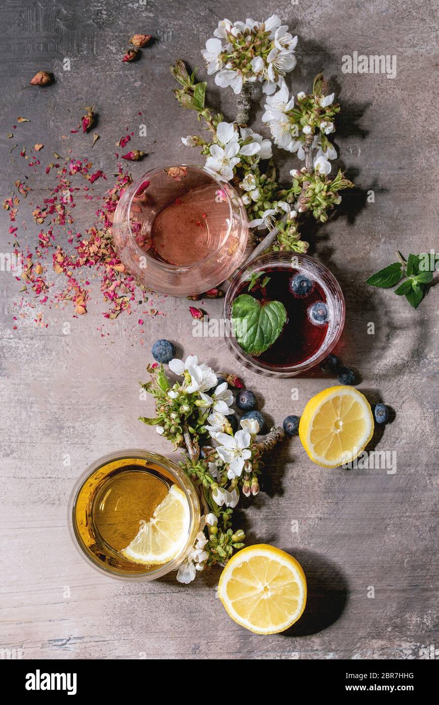 Différents verres à cocktail avec des boissons pétillantes colorées, champagne rose, cidre ou limonade avec boutons de rose secs, citron, bleuets, menthe. Floraison Banque D'Images