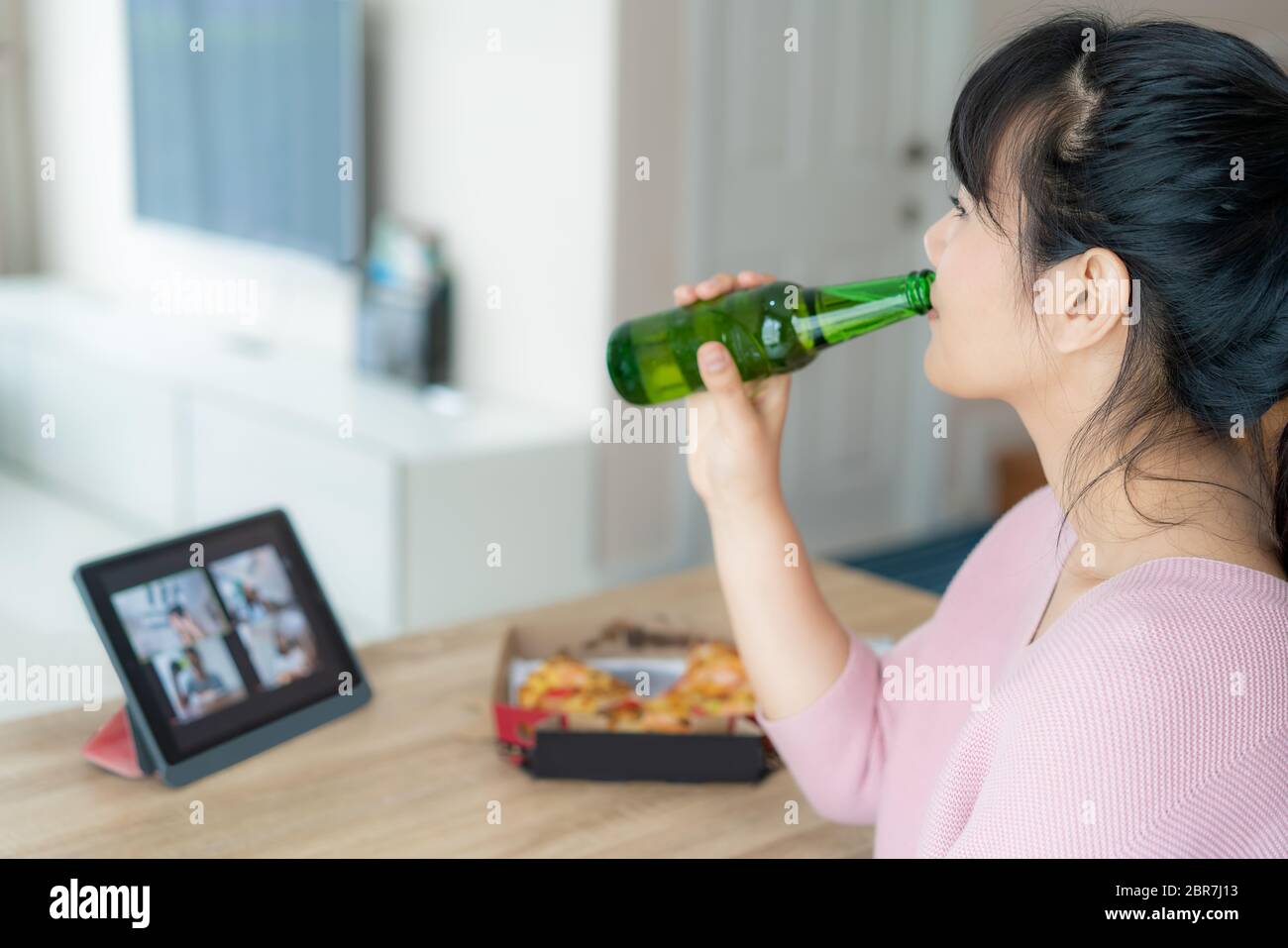Une femme asiatique a une fête virtuelle de happy hour et boire de la bière d'alcool en ligne avec son ami lors d'une visioconférence avec tablette numérique pour un o Banque D'Images