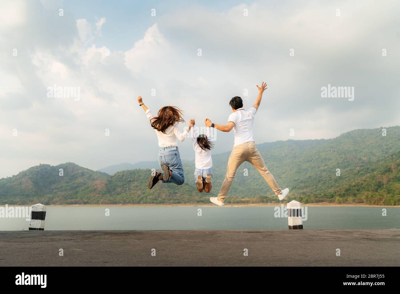 Famille asiatique heureuse avec père, mère et fille sautant dans la route avec vue sur le lac et la montagne en arrière-plan pendant les vacances ensemble en vacances. Happ Banque D'Images